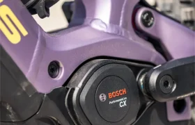 Primer plano de un motor Bosch Performance Line CX instalado en el cuadro de una bicicleta de montaña eléctrica Gama FOCUS e-MTB 2027 de color morado, en el que se aprecia parte de la rueda trasera, lo que permite observar los detalles de las innovadoras series JAM y SAM.