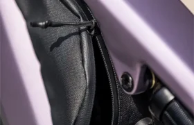 Un primer plano de una pequeña bolsa negra con cremallera fijada al cuadro de una bicicleta eléctrica de montaña (e-MTB) FOCUS de color morado, cerca del tubo superior.