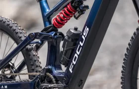 Primer plano de una bicicleta de montaña eléctrica azul FOCUS e-MTB 2027, en el que se aprecian el muelle de la suspensión, la batería y el bidón de agua montados en el cuadro.