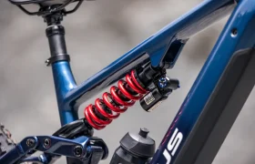 Primer plano del cuadro de una bicicleta eléctrica de montaña (e-MTB) de la marca FOCUS, en el que se aprecian un muelle helicoidal rojo de la suspensión trasera, la tija del sillín, un bidón y parte de la rueda trasera.