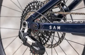Primer plano de la rueda trasera de una bicicleta de montaña, en el que se aprecian el desviador, el cassette, la cadena y parte del cuadro azul marino con la inscripción «SAM», junto con una rueda de las marcas DT Swiss y Schwalbe, lo que permite vislumbrar la ingeniería de precisión que hay detrás de la próxima e-MTB 2027.