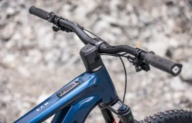 Primer plano del manillar, la potencia y el tubo superior de una bicicleta de montaña eléctrica JAM de color azul, con un fondo de terreno rocoso.