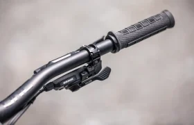 Primer plano del manillar de una bicicleta, con un puño de goma texturizado y una palanca de cambios SRAM con las palancas etiquetadas sobre un fondo gris difuminado, que pone de relieve la ingeniería de precisión del modelo Gama FOCUS e-MTB 2027 JAM.