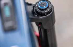 Primer plano de la rueda de ajuste de la horquilla de suspensión de una bicicleta eléctrica de montaña FOCUS e-MTB 2027 junto al cuadro azul de la bicicleta.
