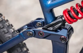 Primer plano del sistema de suspensión trasera de una bicicleta de montaña JAM, en el que se aprecia un muelle helicoidal rojo y componentes del cuadro de color azul.