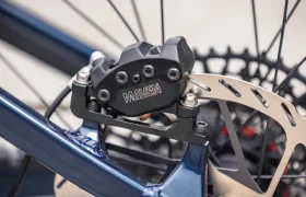 Primer plano de un sistema de frenos de disco para bicicleta en el que se aprecia una pinza de freno MAVEN montada en un cuadro azul de la marca THRON, con un disco metálico fijado a la rueda, ideal para los aficionados a las e-MTB que buscan una potencia de frenado fiable.