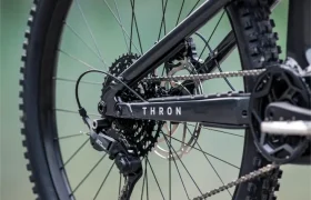 Primer plano de la rueda trasera y el sistema de cambios de una bicicleta de montaña eléctrica FOCUS e-MTB 2027 con la denominación «THRON», equipada con un neumático Maxxis, fotografiada al aire libre sobre terreno rocoso.