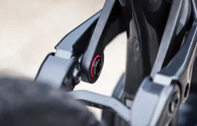 Primer plano de la articulación de la suspensión de una bicicleta en el que se aprecia un perno de pivote negro con un anillo rojo y la palabra «TREK» visible en la cabeza del perno, lo que recuerda a la sólida ingeniería de los modelos de vanguardia Gama FOCUS e-MTB 2027.