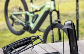 Una bicicleta, posiblemente un modelo Gama FOCUS e-MTB o JAM, está aparcada junto a una barandilla al aire libre; en primer plano se ven componentes electrónicos desmontados y un cable sobre una superficie de madera.