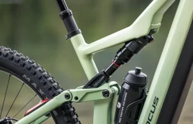 Primer plano del cuadro de una bicicleta de montaña eléctrica FOCUS e-MTB 2027 de color verde claro, en el que se aprecian el sistema de suspensión trasera, la rueda trasera y un bidón negro fijado al cuadro.
