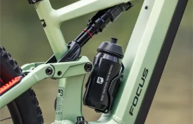 Primer plano del cuadro de una bicicleta de montaña eléctrica FOCUS e-MTB de color verde claro, en el que se aprecian el compartimento de la batería, la suspensión, la biela, la cadena y un bidón negro fijado al cuadro.