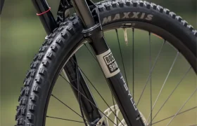 Primer plano de la rueda delantera de una bicicleta de montaña en el que se aprecian una horquilla de suspensión RockShox, un disco de freno y un neumático Maxxis al aire libre: ideal para afrontar cualquier sendero con la gama de bicicletas eléctricas de montaña Gama FOCUS, incluidos modelos tan populares como la JAM y la SAM.