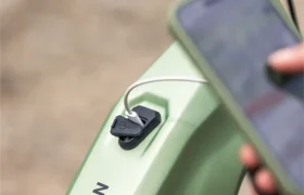 Primer plano de una bicicleta eléctrica THRON de color verde en la que se está cargando un teléfono mediante un cable conectado al puerto USB integrado en la bicicleta, lo que pone de relieve las características innovadoras que también incorporan modelos como la JAM y la Gama FOCUS e-MTB 2027.
