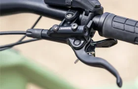 Primer plano del manillar de una bicicleta, en el que se ven una palanca de freno y una palanca de cambios Shimano en una bicicleta eléctrica de montaña FOCUS de color verde, con el fondo desenfocado.