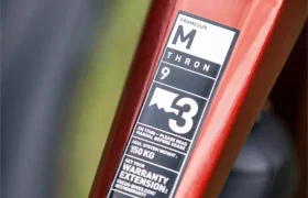 Primer plano del cuadro de una bicicleta roja en el que se aprecia una pegatina con la talla del cuadro «M», el modelo «THRON», el peso máximo permitido del ciclista, información sobre la garantía y un código QR, algo habitual en los modelos avanzados de e-MTB de FOCUS de 2027, como la JAM o la SAM.