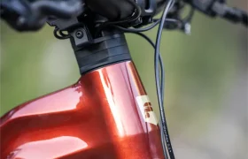 Primer plano de la parte delantera de una bicicleta eléctrica de montaña (e-MTB) de color rojo metalizado, en el que se aprecian el manillar, los cables y parte de la horquilla delantera.