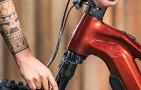 Primer plano de dos personas ajustando la horquilla de suspensión delantera de una bicicleta de montaña JAM roja; una de ellas señala la horquilla, mientras que la otra sujeta el manillar.