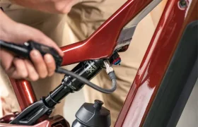 Primer plano de una persona que sostiene un teléfono junto al cuadro rojo de una bicicleta eléctrica de montaña (e-MTB) de la marca FOCUS, en el que se aprecian el portabidón y el sistema de suspensión.