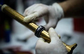 Una persona que lleva guantes coloca un anillo negro en un tubo metálico de color dorado, que podría formar parte de un componente mecánico o de automoción.
