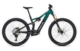 Una bicicleta de montaña Focus e-MTB 2027 de doble suspensión, de color verde y negro, con neumáticos gruesos y con relieve, frenos de disco y un motor eléctrico visible montado en el cuadro.