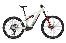 Una bicicleta de montaña eléctrica FOCUS e-MTB de suspensión total, en colores blanco y rojo, con neumáticos de tacos, frenos de disco y el logotipo de Focus en el cuadro; se muestra de perfil sobre un fondo blanco. Ideal para los aficionados a las series JAM o SAM que buscan tanto estilo como rendimiento.