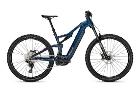 Se muestra una vista de perfil lateral de una bicicleta eléctrica de montaña (e-MTB) azul del modelo 2027, con suspensión total, frenos de disco, un motor de tracción central y neumáticos con tacos.