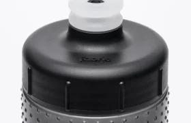 Primer plano de la parte superior de una botella de agua negra con textura y una boquilla translúcida que se levanta para beber. La palabra «fabric» aparece grabada en relieve en la botella, justo debajo del tapón, lo que resalta el elegante diseño del bidón antimicrobiano Fabric Gripper V2, que ofrece protección permanente.