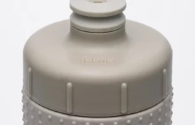 Primer plano de una tapa para botella de agua «Fabric Gripper V2» de color gris claro, con una boquilla de tipo «push-pull» y una textura de puntos en relieve en la parte superior de la botella; la palabra «fabric» aparece grabada en relieve en la tapa, lo que destaca sus propiedades antimicrobianas para una protección permanente.