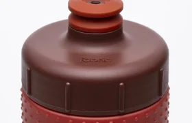 Primer plano de la parte superior de una botella de agua «Fabric Gripper V2» de color rojo y marrón, con un agarre texturizado y una boquilla de tipo «push-pull», que ofrece protección permanente gracias a su diseño antimicrobiano.