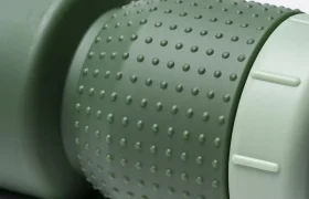 Primer plano de una botella de plástico verde con textura y agarre estriado, que incorpora el innovador diseño «Fabric Gripper V2» para facilitar su manejo. Esta botella antimicrobiana ofrece protección permanente y cuenta con un tapón de rosca de color verde claro, todo ello sobre un fondo liso.