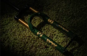 Una horquilla de suspensión FOX 38 Racing Green con detalles dorados descansa sobre musgo verde, parcialmente iluminada por la luz.