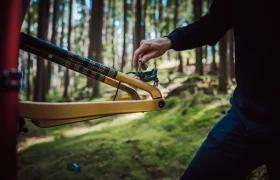 Una persona ajusta el cambio trasero de una bicicleta de montaña amarilla equipada con un FOX 38 Racing Green Edición Limitada en un sereno entorno forestal.