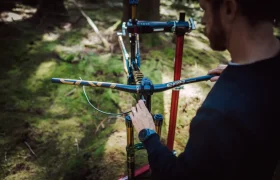 Una persona ajusta el manillar de una bicicleta de montaña con horquilla FOX 38 Racing Green Edición Limitada, montada en un soporte de reparación en una zona boscosa.