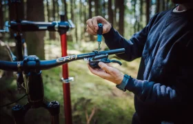 Una persona ajusta el manillar de una bicicleta con un destornillador al aire libre en una zona boscosa, con la FOX 38 Racing Green Edición Limitada.