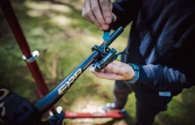 Persona apretando tornillos en un manillar de bicicleta utilizando una herramienta azul, centrándose en el ajuste de la palanca de freno de una FOX 38 Racing Green en un entorno al aire libre.