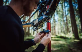 Una persona examina un componente de bicicleta FOX 38 Racing Green Edición Limitada mientras se encuentra en una zona boscosa, con la bicicleta montada en un soporte de reparación.