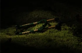 Una horquilla de suspensión de bicicleta de montaña FOX 38 Racing Green Edición Limitada descansa sobre un suelo musgoso, parcialmente iluminada por un haz de luz en un entorno por lo demás oscuro.