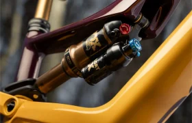 Primer plano del sistema de suspensión trasera de una bicicleta de montaña, con amortiguadores FOX con pomos de ajuste y parte del cuadro de la bicicleta X Factor en amarillo y granate.