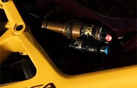 Primer plano de un amortiguador trasero Fox instalado en un cuadro amarillo de bicicleta de montaña, mostrando la marca X Factor y amortiguadores FOX de nueva generación con diales de ajuste claramente visibles.