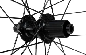 Primer plano de un buje negro de rueda trasera de bicicleta Shimano con radios que irradian hacia fuera, visto desde un ángulo.