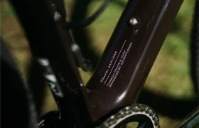 Primer plano de un cuadro de bicicleta Van Rysel RCR-G de color marrón, en el que se aprecia, cerca del juego de bielas, el texto «Gravel Explore, cuadro de carbono, diseñado por aventureros».