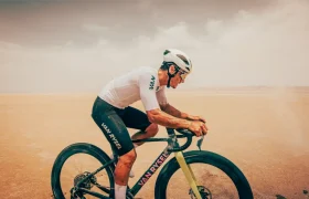Un ciclista, con casco y maillot blancos, recorre un paisaje seco y arenoso a lomos de una bicicleta de gravel Van Rysel RCR-G, bajo un cielo brumoso.