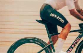 Un ciclista, vestido con ropa de competición, pedalea en una bicicleta Van Rysel RCR-G sobre una superficie de grava arenosa y difuminada, lo que resalta el movimiento y la velocidad.
