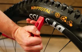Una persona utiliza una palanca roja para desmontar una cubierta de MTB Continental Gravity con la inscripción «KRYPTOTAL» de una rueda con la marca «DT SWISS», en un espacio interior.