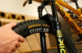 Una persona sostiene la rueda delantera de una bicicleta de montaña con las marcas «Kryptotal» y «DT Swiss», con especial atención a los neumáticos Continental para MTB y a la horquilla de suspensión Gravity.