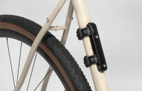 Primer plano de la parte trasera de una bicicleta con cuadro beige, con un accesorio Tailfin Hydromount montado verticalmente cerca de la rueda trasera.