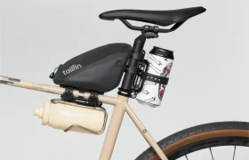 Vista lateral de un cuadro de bicicleta beige con un sillín negro, una bolsa Tailfin, una botella de agua blanca en una jaula en el cuadro y una lata en una jaula Tailfin Hydromount detrás de la tija del sillín.