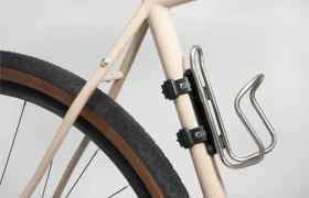 Primer plano de un cuadro de bicicleta beige que muestra la rueda trasera con neumático de tacos y un portabidón Tailfin Hydromount fijado al cuadro.