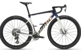 La BMC Kaius 01 es una bicicleta avanzada con un cuadro blanco, azul y negro, manillar rebajado, frenos de disco y neumáticos gruesos, sobre un fondo blanco.