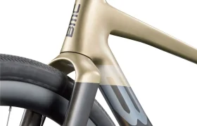 Primer plano de la horquilla delantera y el cuadro de una bicicleta rápida, en el que se aprecia el logotipo de BMC y parte de la rueda delantera, destacando el elegante diseño de la BMC Kaius 01, una bicicleta actual sobresaliente.